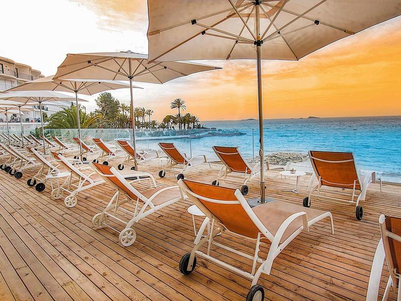 Strand mit Holzsteg, Liegestühlen und Sonnenschirmen bei Sonnenuntergang am Meer.