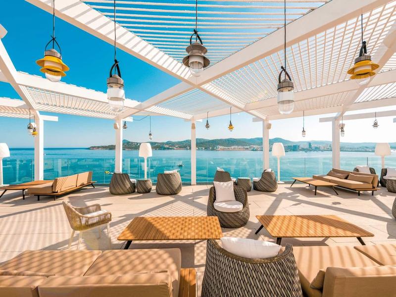 Area lounge all'aperto con mobili da terrazza e vista sul mare sotto una pergola bianca.