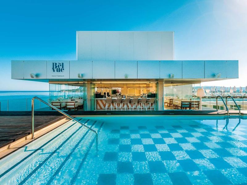 Piscina d'hotel moderna con disegno del pavimento geometrico e facciata in vetro sotto un cielo limpido.