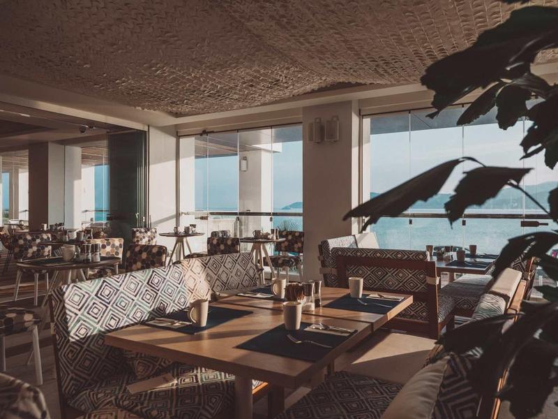 Ristorante moderno con tavoli e sedie in legno con vista sul mare attraverso grandi finestre.