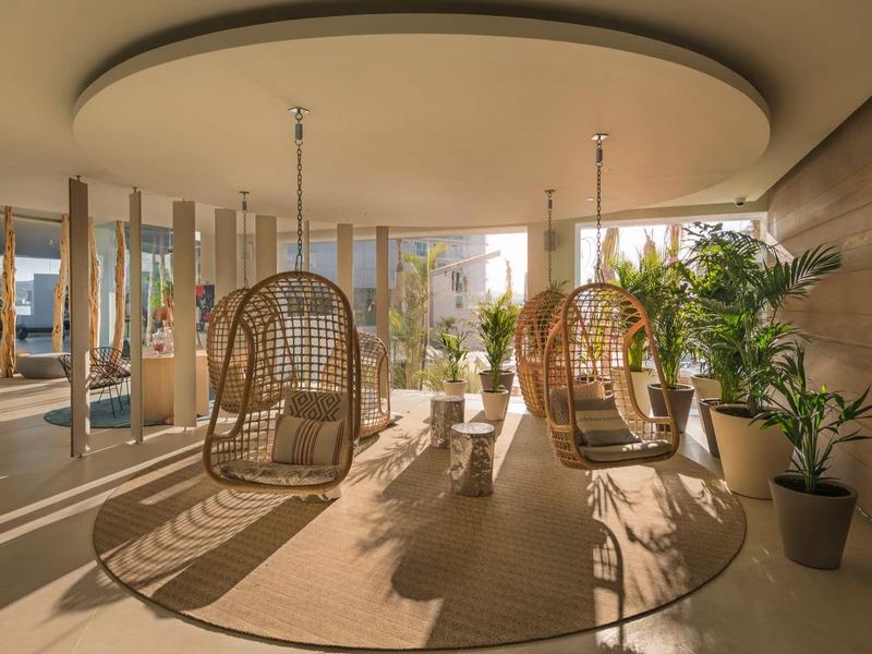 Spazio interno moderno con sedie sospese in rattan e piante, luce solare che entra.