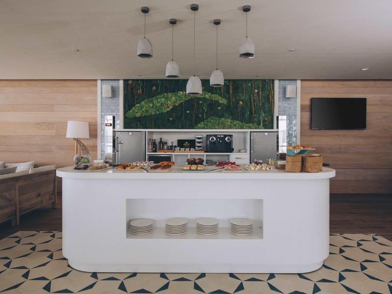 Bar dell'hotel moderna con bancone bianco, pannelli in legno e pavimento piastrellato.