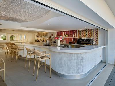 Bar lumineuse avec tabourets en bois et décoration moderne dans un espace hôtelier ouvert.