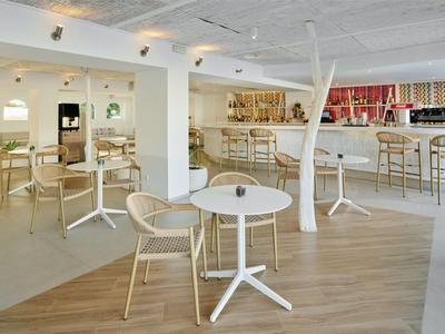 Espace bar d'hôtel moderne avec tables blanches, chaises en bois et un long comptoir en arrière-plan.