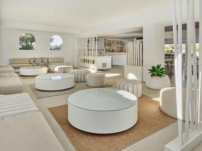 Salon lumineux avec mobilier blanc, tables rondes et coussins dans un intérieur d'hôtel moderne.