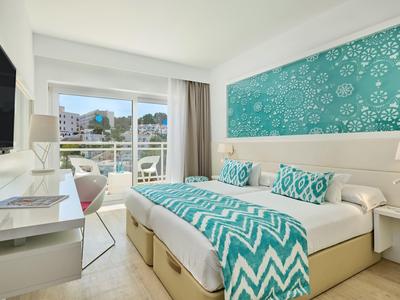 Chambre d'hôtel moderne avec lit double, literie turquoise et balcon avec vue sur la ville.