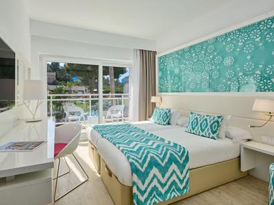 Chambre d'hôtel moderne avec lit double, accents turquoise et balcon donnant sur la verdure.