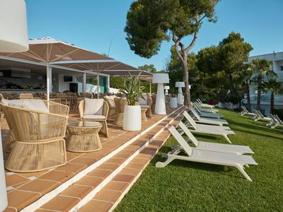 Terrasse avec chaises longues et sièges ronds en osier à côté du bâtiment de l'hôtel sur pelouse verte sous des arbres.