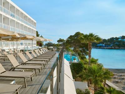 Terrasse d'hôtel avec chaises longues donnant sur la piscine et la mer sous un ciel clair.