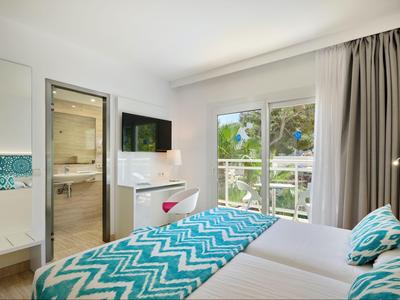 Chambre d'hôtel lumineuse avec lit double, motif turquoise, télévision et balcon donnant sur le jardin.