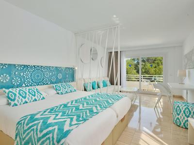 Chambre d'hôtel lumineuse avec lit double, textiles bleu-blanc et balcon avec vue sur la verdure.