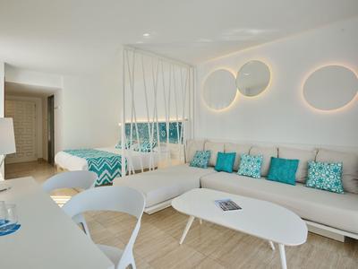 Salon lumineux avec mobilier blanc, accents turquoise et lampes murales modernes dans un hôtel.
