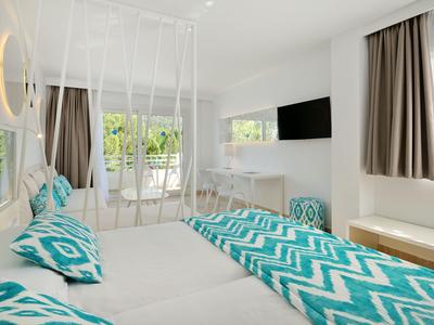 Chambre d'hôtel lumineuse avec deux lits, textiles turquoise à motifs et grandes fenêtres avec rideaux.