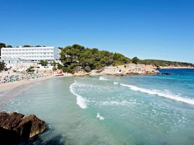 Strand mit Hotel, blauem Himmel und klarem Wasser in einer ruhigen Bucht.