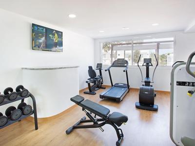 Heller Fitnessraum mit Laufbändern, Hanteln und Trainingsgeräten auf Holzfußboden.