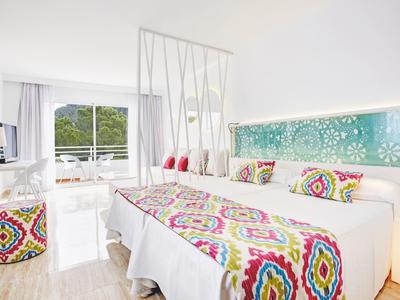 Helles Hotelzimmer mit zwei Betten, bunten Kissen und Decken, Balkon und moderner Einrichtung.