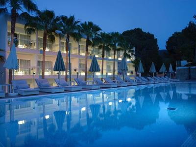 Beleuchteter Hotelpool mit Liegestühlen und Sonnenschirmen bei Nacht.
