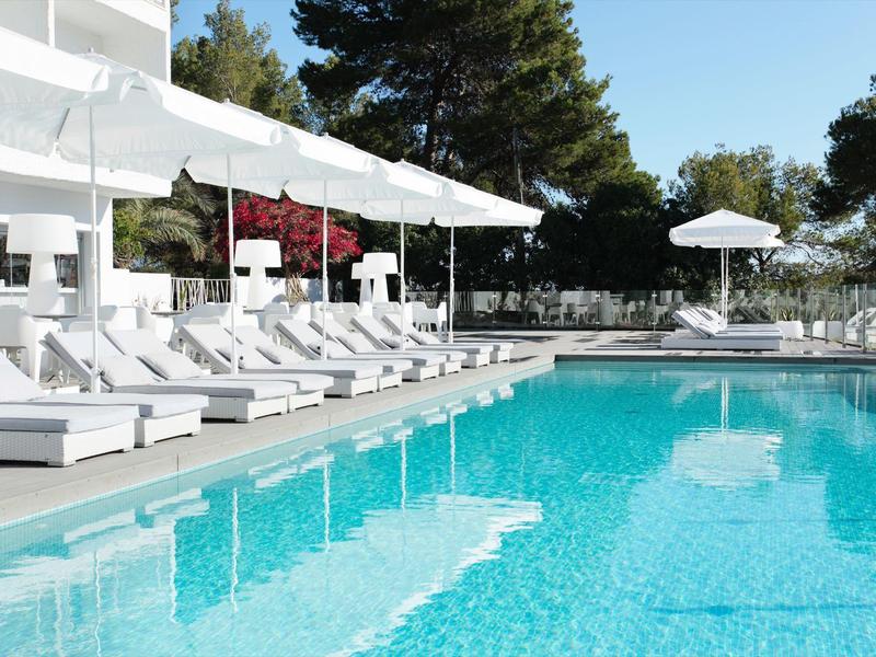 Moderner Hotelpool mit weißen Liegestühlen und Sonnenschirmen an einem sonnigen Tag.