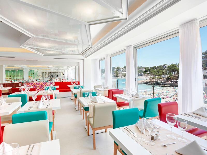 Helles Restaurant mit bunten Stühlen und großen Fenstern mit Blick auf das Meer.