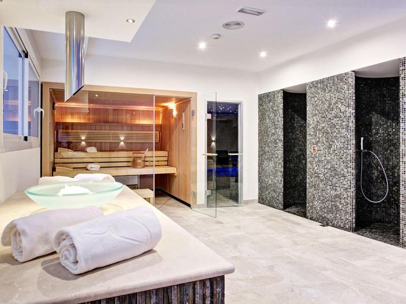 Moderner Wellnessraum mit Sauna, drei Duschen und Liege mit Handtüchern.