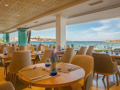 Hell eingerichtetes Restaurant mit Holztischen, bequemen Stühlen und großer Meeresblick-Terrasse.