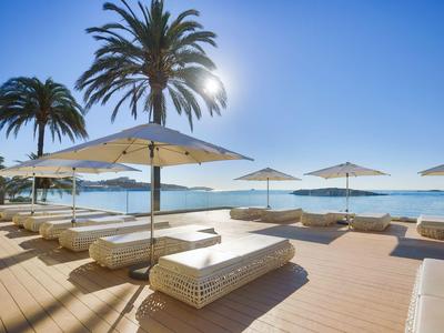 Plážová lehátka s slunečníky na dřevěné terase u moře za slunného dne.