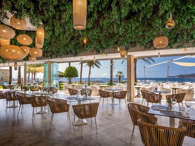 Ristorante aperto con vista mare, soffitto verde e arredi naturali.
