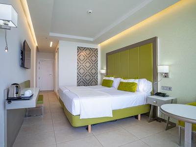 Camera d'hotel moderna con letto grande, testiera verde e biancheria bianco-verde.