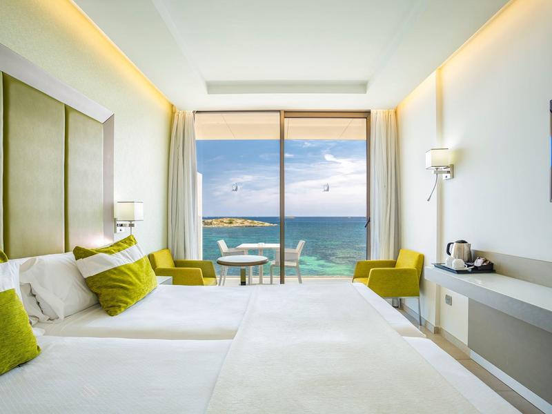 Camera d'hotel moderna con letto matrimoniale e vista mare attraverso grandi finestre.