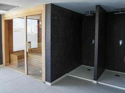 Moderne Sauna mit Holzverkleidung und zwei offenen Duschkabinen mit schwarzen Fliesen.