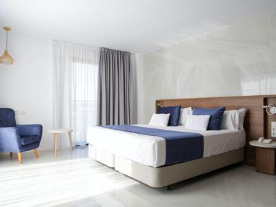 Modern hotel room with large bed, blue and white pillows, and a blue armchair by the window.