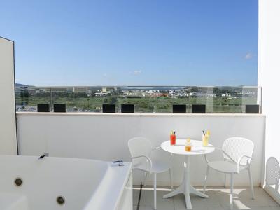 Terrasse mit weißem Whirlpool, rundem Tisch, zwei Stühlen und weitem Blick auf die Landschaft.