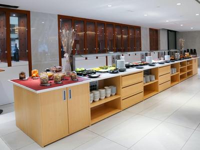 Buffet mit Holzschränken, Teller, Schüsseln und verschiedenen Speisen in hellem Raum.