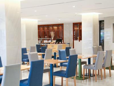 Moderner, heller Gastraum mit blauen und grauen Stühlen, Holztischen und weißem Marmorboden.