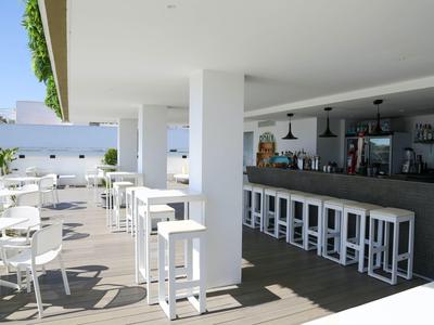 Area bar esterna moderna con tavoli, sedie e sgabelli bianchi su terrazza in legno.