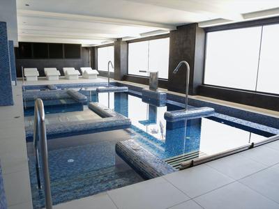 Moderner Innenpool mit blauen Fliesen, Wasserfunktion und Liegestühlen am Fensterbereich.