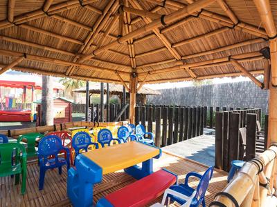 Überdachter Außenbereich mit bunten Kindertischen und -stühlen aus Kunststoff unter Holzdach.