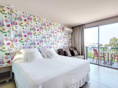 Schlafzimmer mit großem Bett, Blumentapete, bequemen Stühlen und Balkon mit Aussicht.