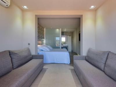 Modern eingerichtetes Zimmer mit zwei grauen Sofas, einem Bett und Glaswand zum angrenzenden Bereich.