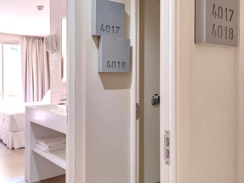 Flur mit weißen Wänden, Zimmertüren und grauen Raumnummern, Licht von einem hellen Raum.