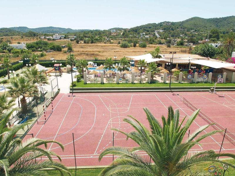 Rotes Basketballfeld mit Palmen vorne, grünen Hügeln im Hintergrund und Sonnenschirmen am Rand.