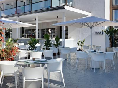 Moderner Außenbereich eines Hotels mit weißen Tischen, Stühlen und Sonnenschirmen.