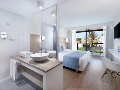 Modernes Hotelzimmer mit großem Fenster, Doppelbett und offenem Badbereich in hellem Holzton.
