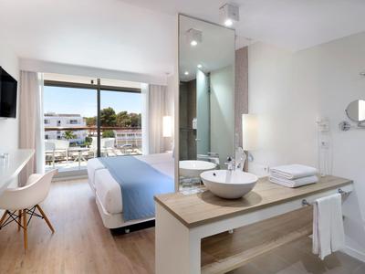Modernes Hotelzimmer mit Bett, Badezimmerwaschbecken und Balkon mit Meerblick.