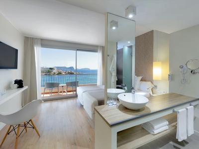 Modernes Hotelzimmer mit Doppelbett, Balkon und Meerblick, offenem Bad mit Waschbecken.