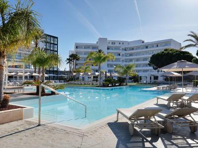 Moderner Hotelpool mit Liegestühlen, Palmen und Sonnenschirmen bei klarem Himmel.