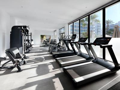 Heller Fitnessraum mit Laufbändern und Kraftgeräten vor großen Fenstern und Bergblick.