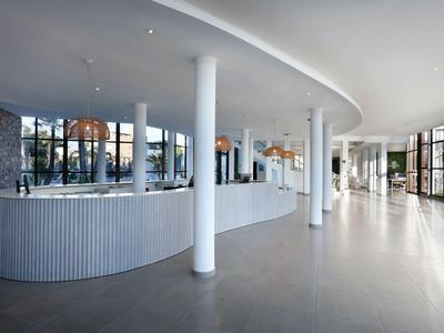 Heller, moderner Hotellobby mit großer Rezeption, weißen Säulen und bodentiefen Fenstern.