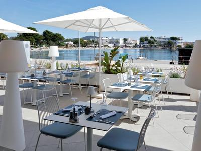 Moderner Außenbereich eines Hotels mit weißen Sonnenschirmen und Blick auf das Wasser.