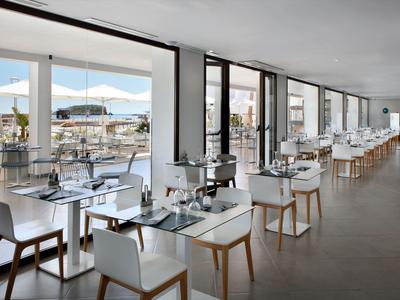 Hell eingerichtetes Hotelrestaurant mit Glaswänden und Blick auf Terrasse mit Sonnenschirmen.